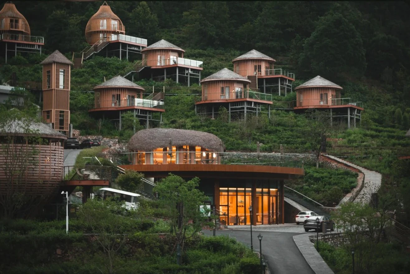 Modular guest cabins lit at dusk across a wooded mountain resort